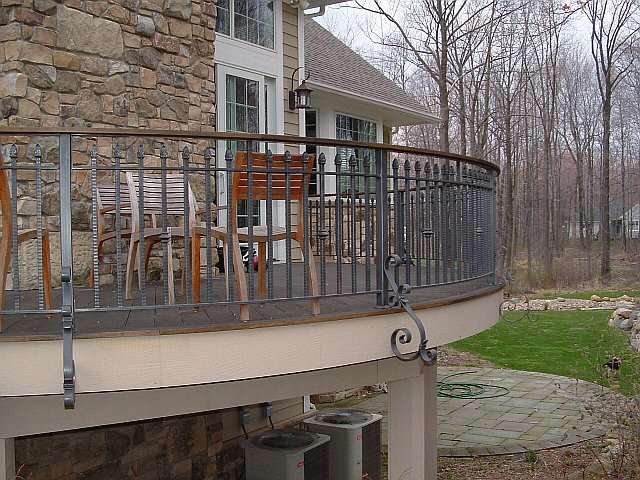 Outdoor iron railing surrounds an elevated stone and brick patio in this landscape design.